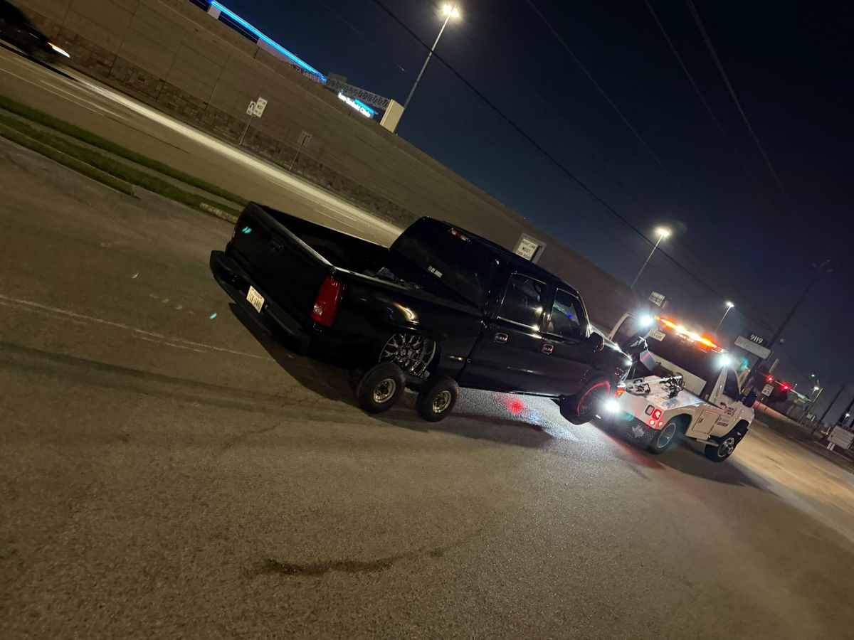 A black truck being towed by a tow truck at night on a Houston road