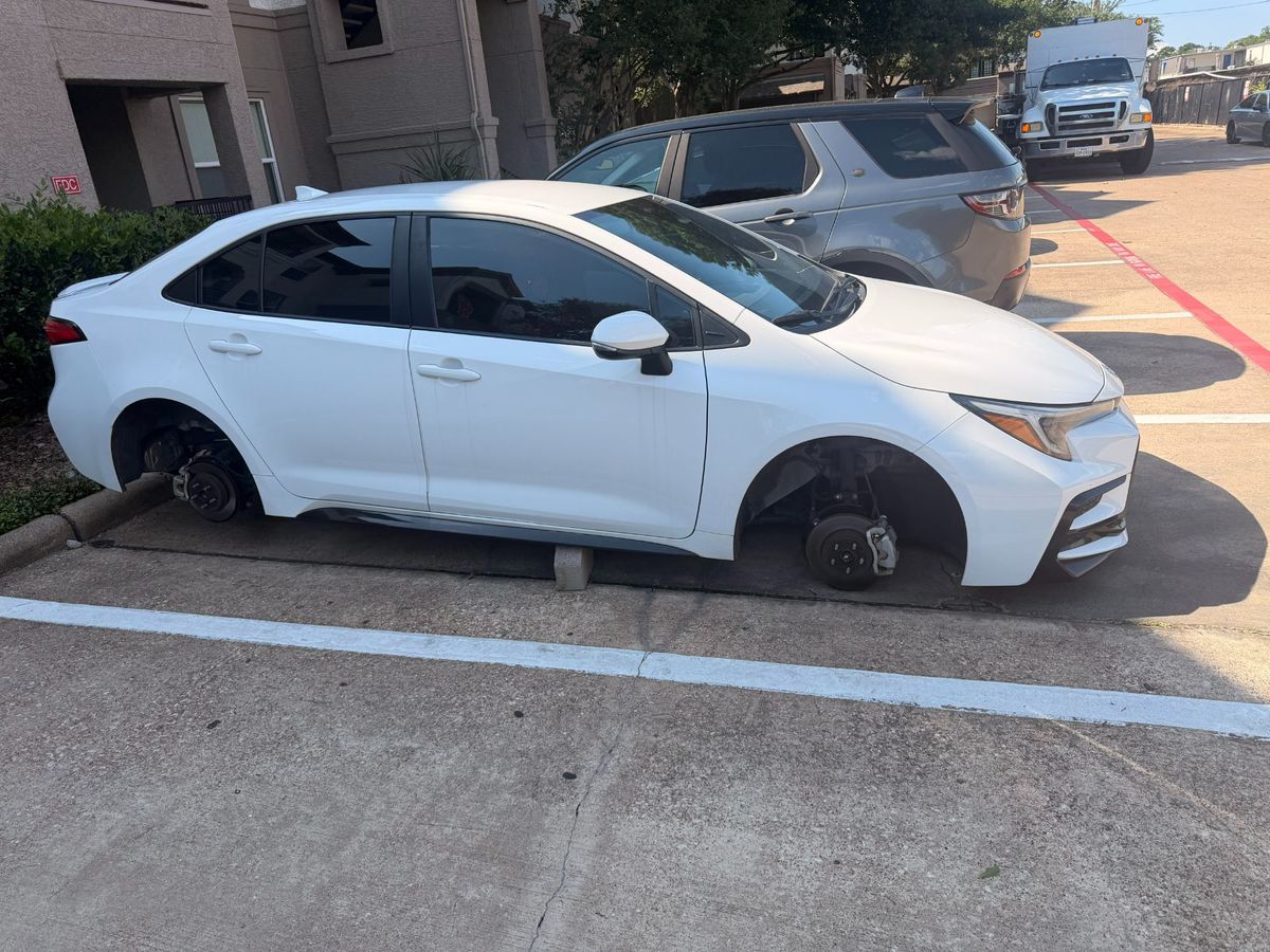 White car parked on a driveway missing wheels, indicating the need for flat tire assistance from Turbo Tows after their wheels got stolen