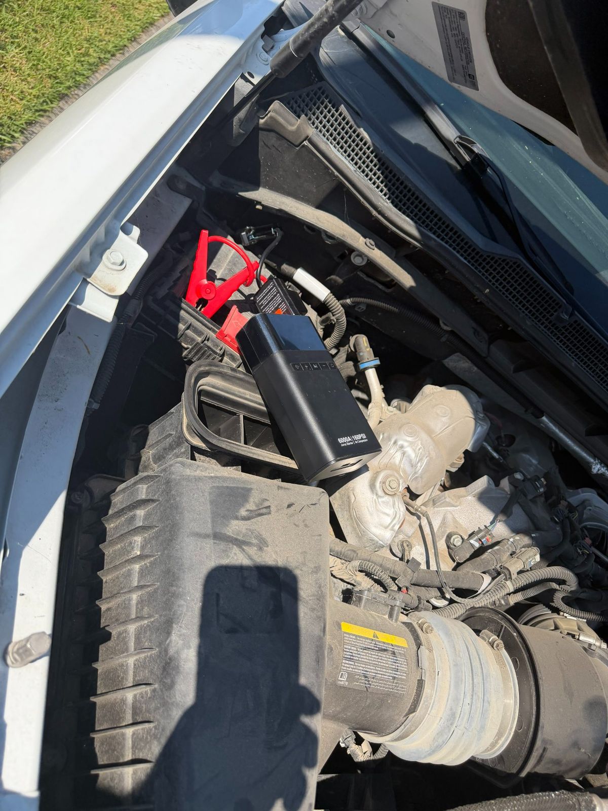 An engine bay with a jump starter and battery connections during a roadside assistance service.