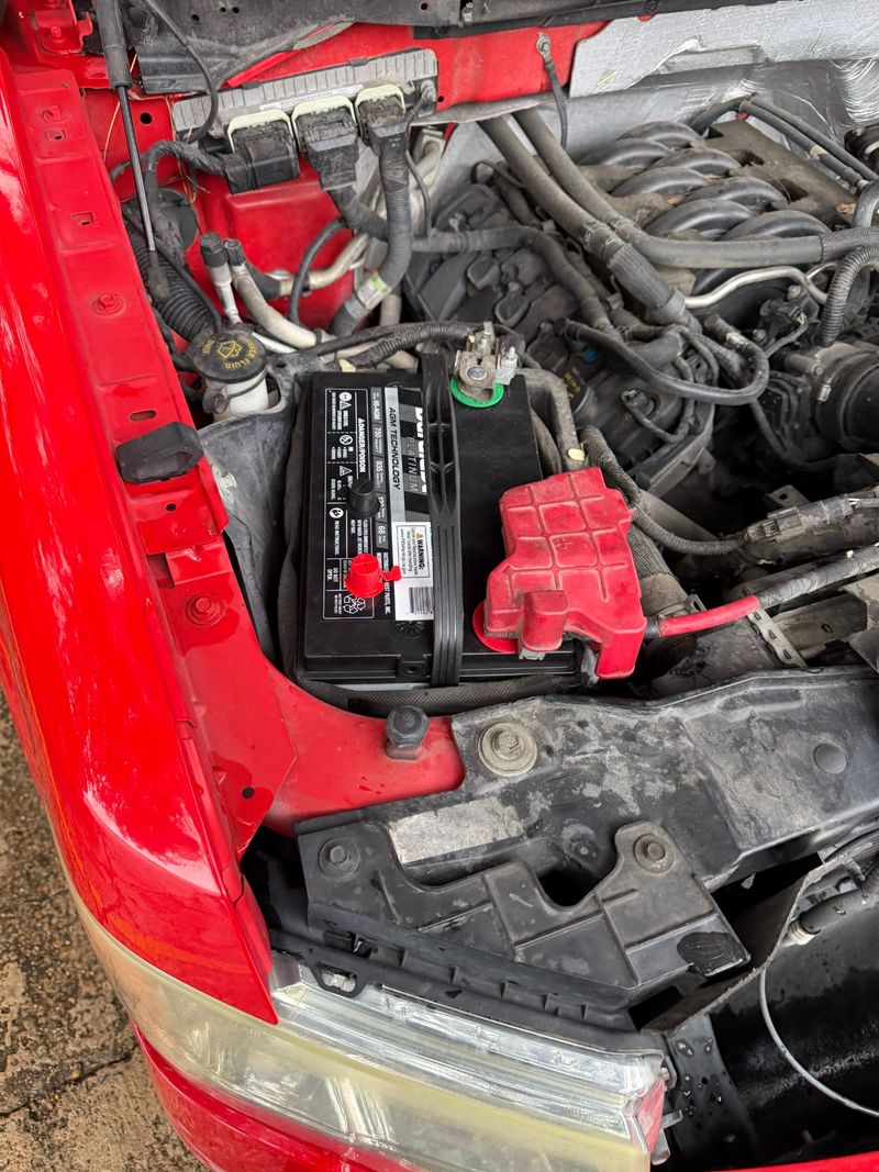 Close-up image of a car battery and engine components in a vehicle's hood, indicating roadside assistance services.
