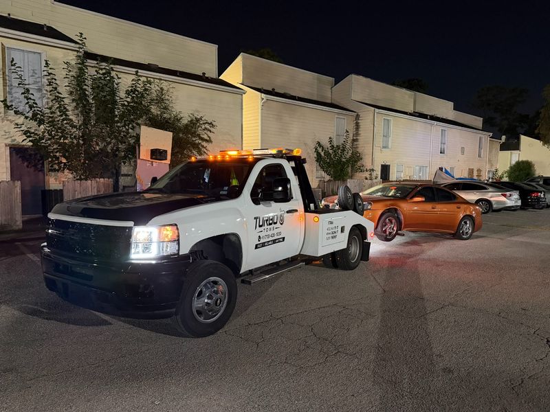 Turbo Tows truck towing an orange car for a cheap price at night in Houston.
