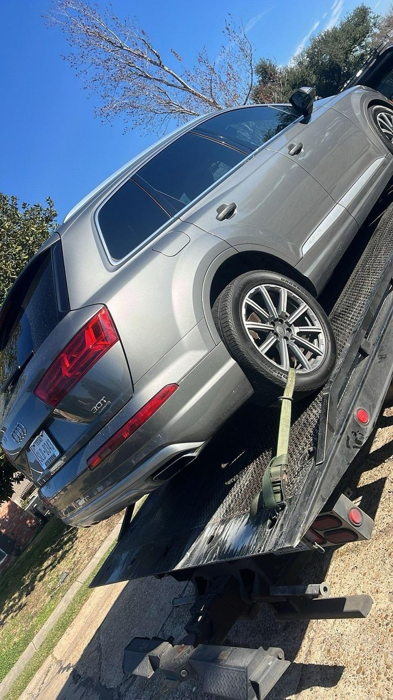 A grey Audi SUV being loaded onto a tow truck on a sunny day, showcasing Turbo Tows emergency towing service.