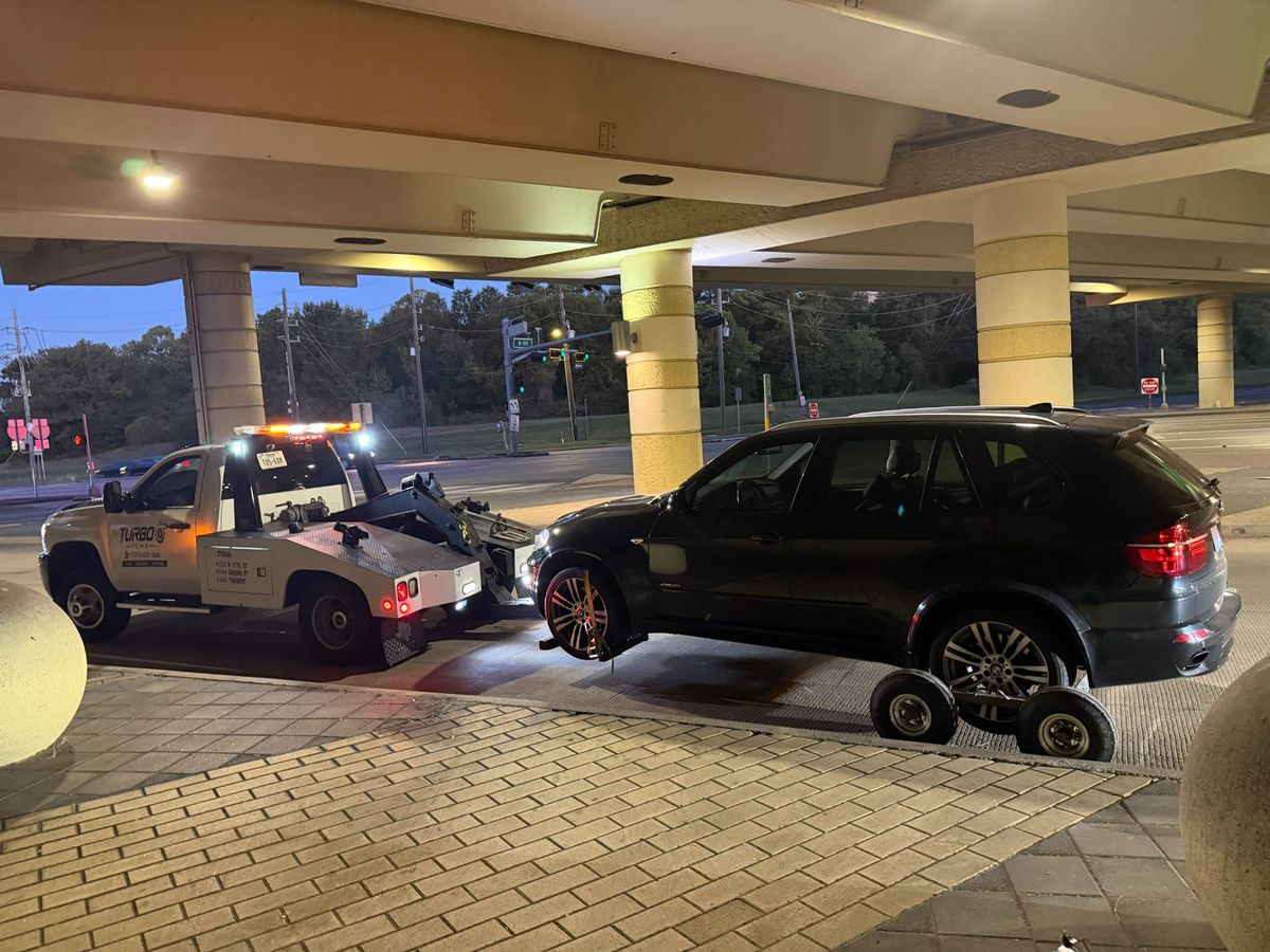 A tow truck from Turbo Tows assisting a black SUV at night in Houston, showcasing the emergency towing service for all wheel drive cars.