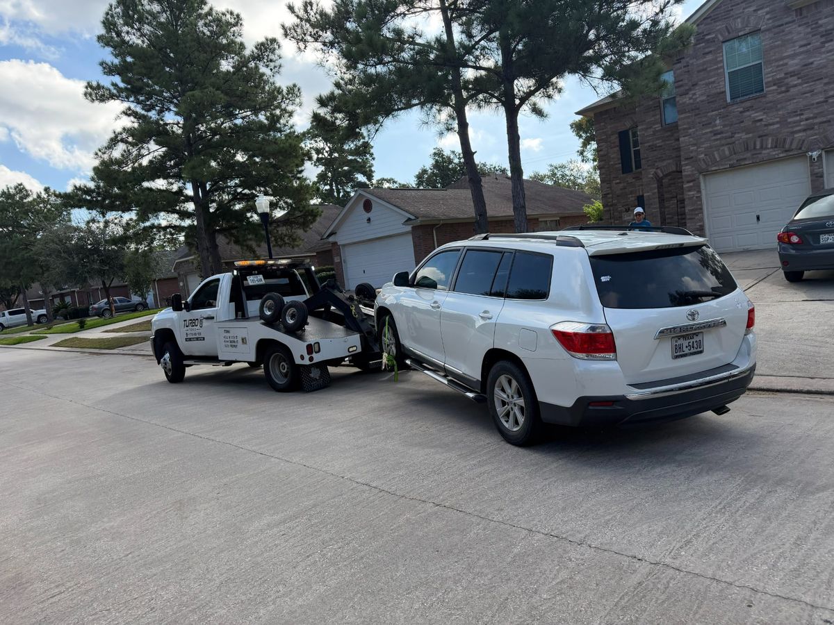 A Turbo Tows vehicle towing a white SUV on a residential street in Houston.