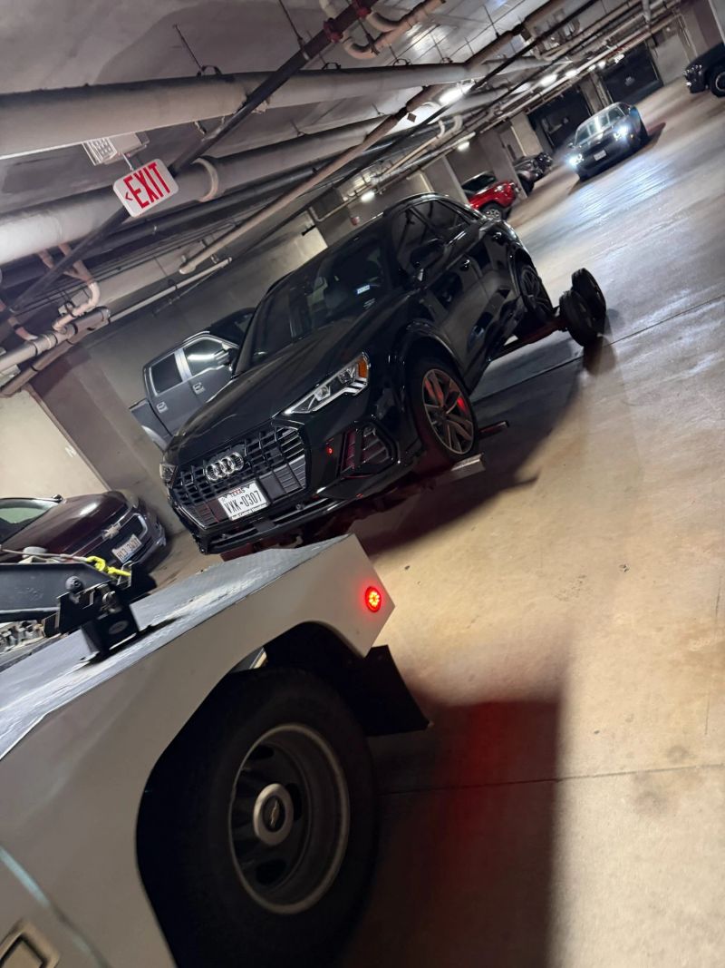 A black Audi being towed by Turbo Tows in a low clearance parking garage, showcasing emergency towing services.