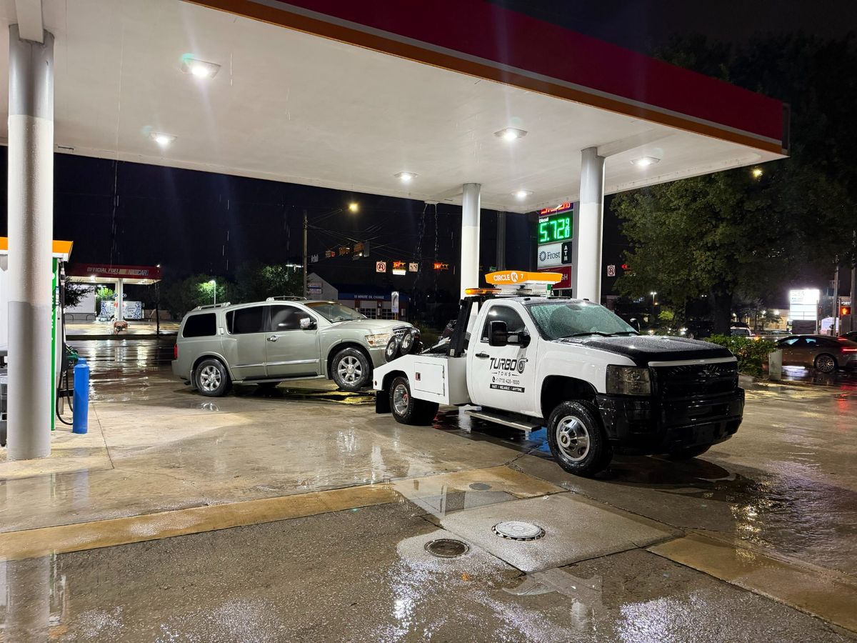 Turbo Tows truck assisting a vehicle at a gas station in Houston on a rainy night.