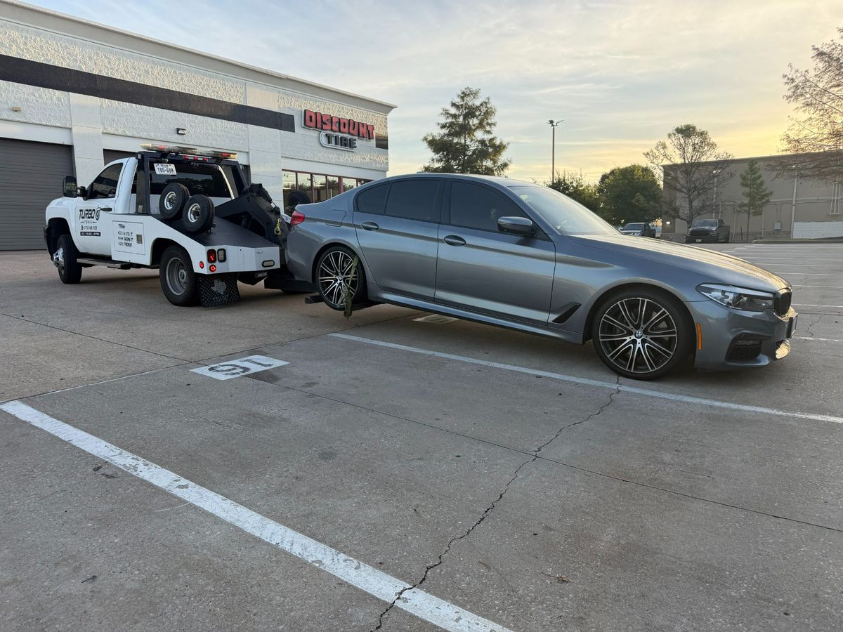 Tow truck lifting a silver car in a parking lot outside Discount Tire in Houston.
