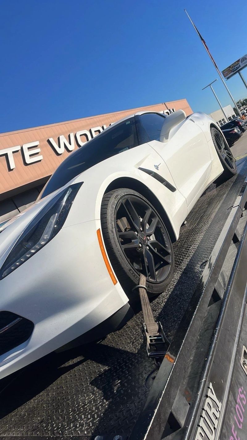A white sports car on a flatbed tow truck platform under a clear blue sky, with Turbo Tows signage in the background.